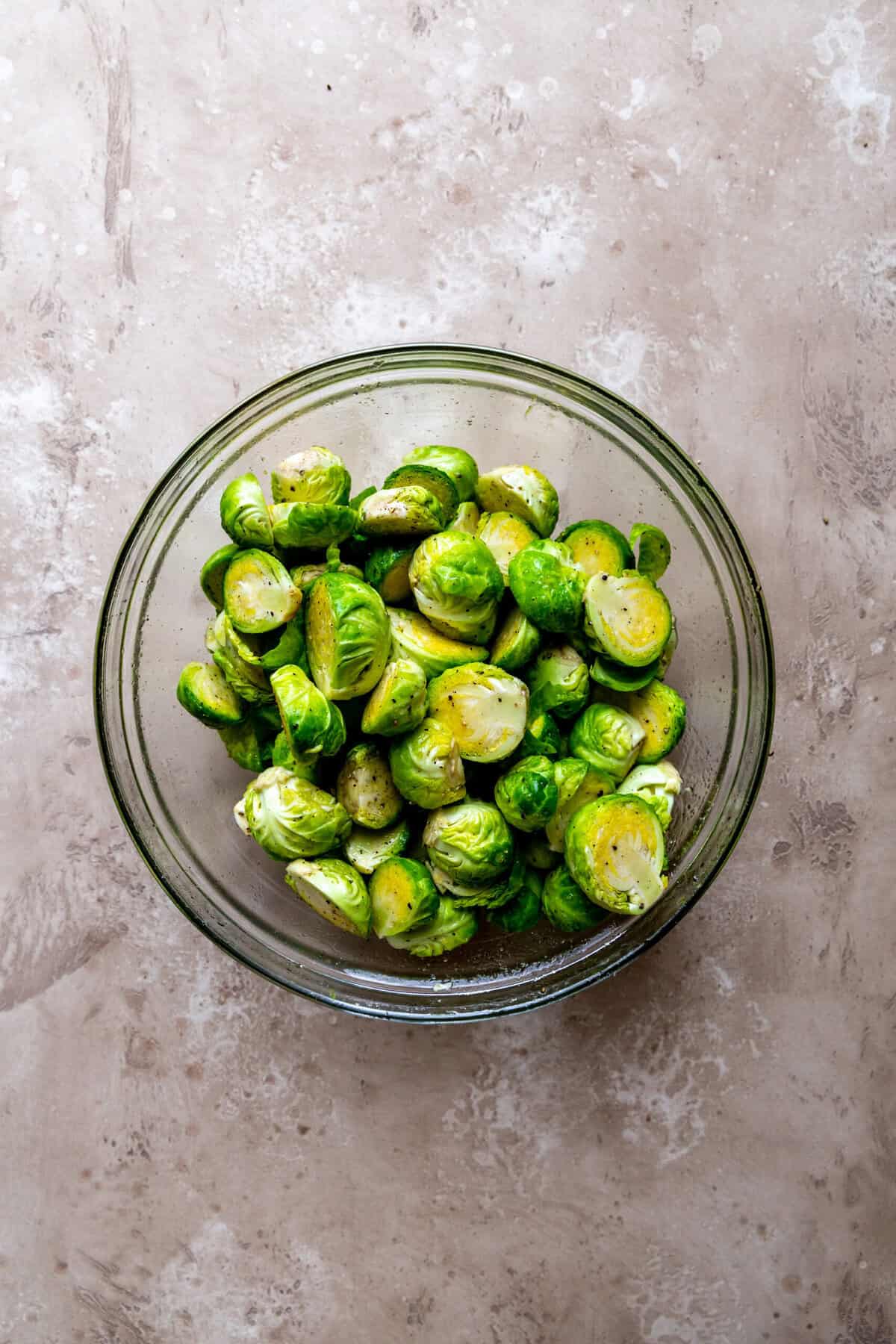 Brussels sprout halves tossed in oil and spices in a glass bowl.