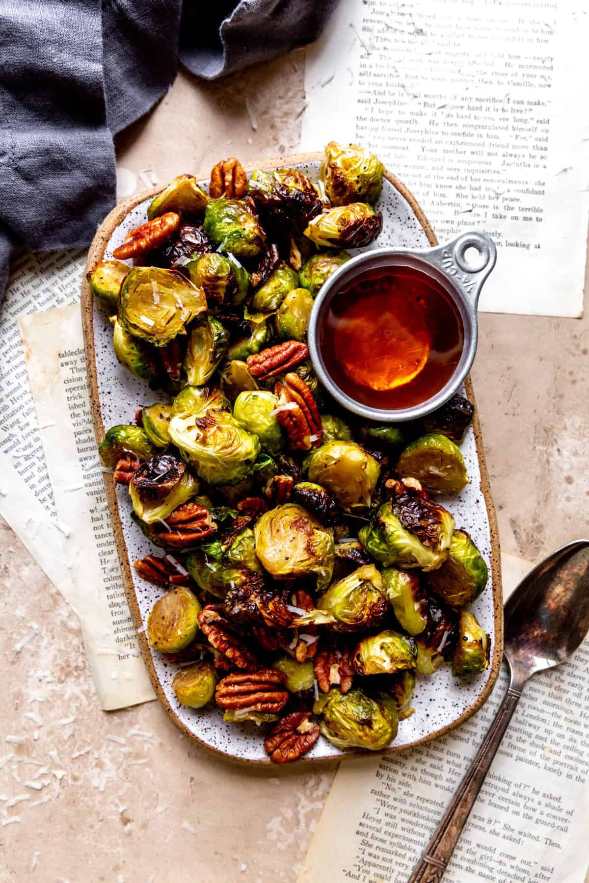 Roasted brussels sprouts on a serving dish with a cup of maple syrup.