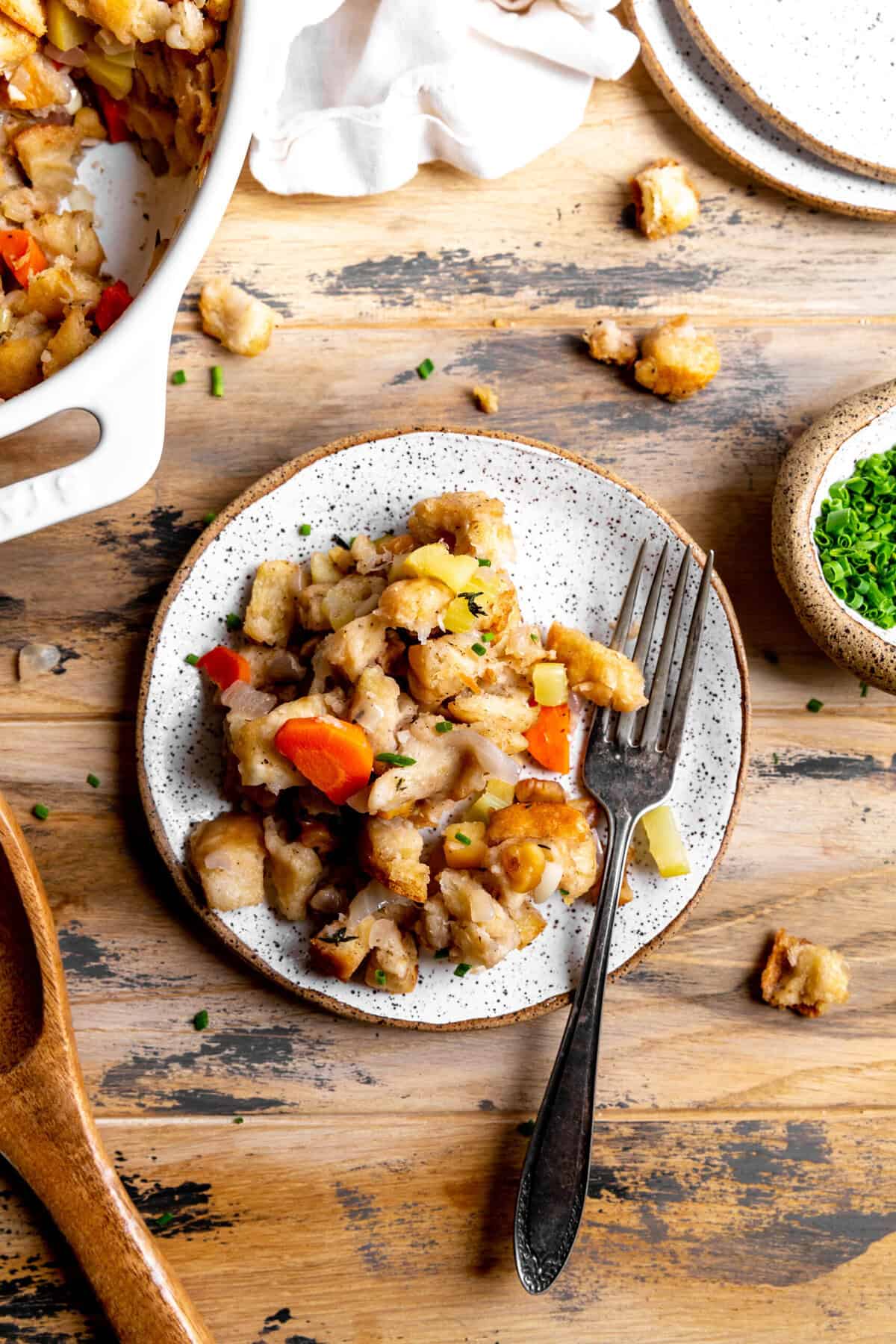 Plate of vegan stuffing with a fork and a small cup of chopped chives.