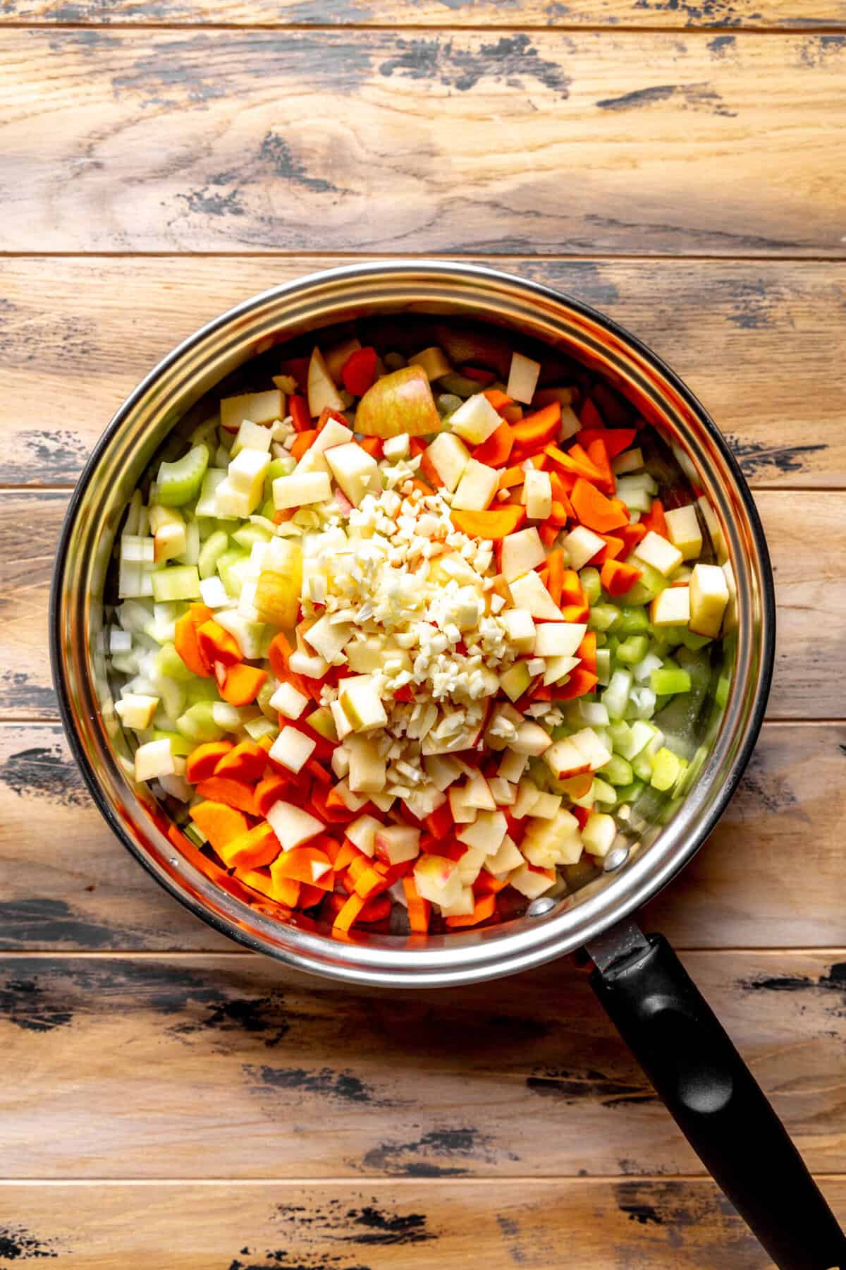Skillet full of chopped onion, celery, carrots, apple and garlic.