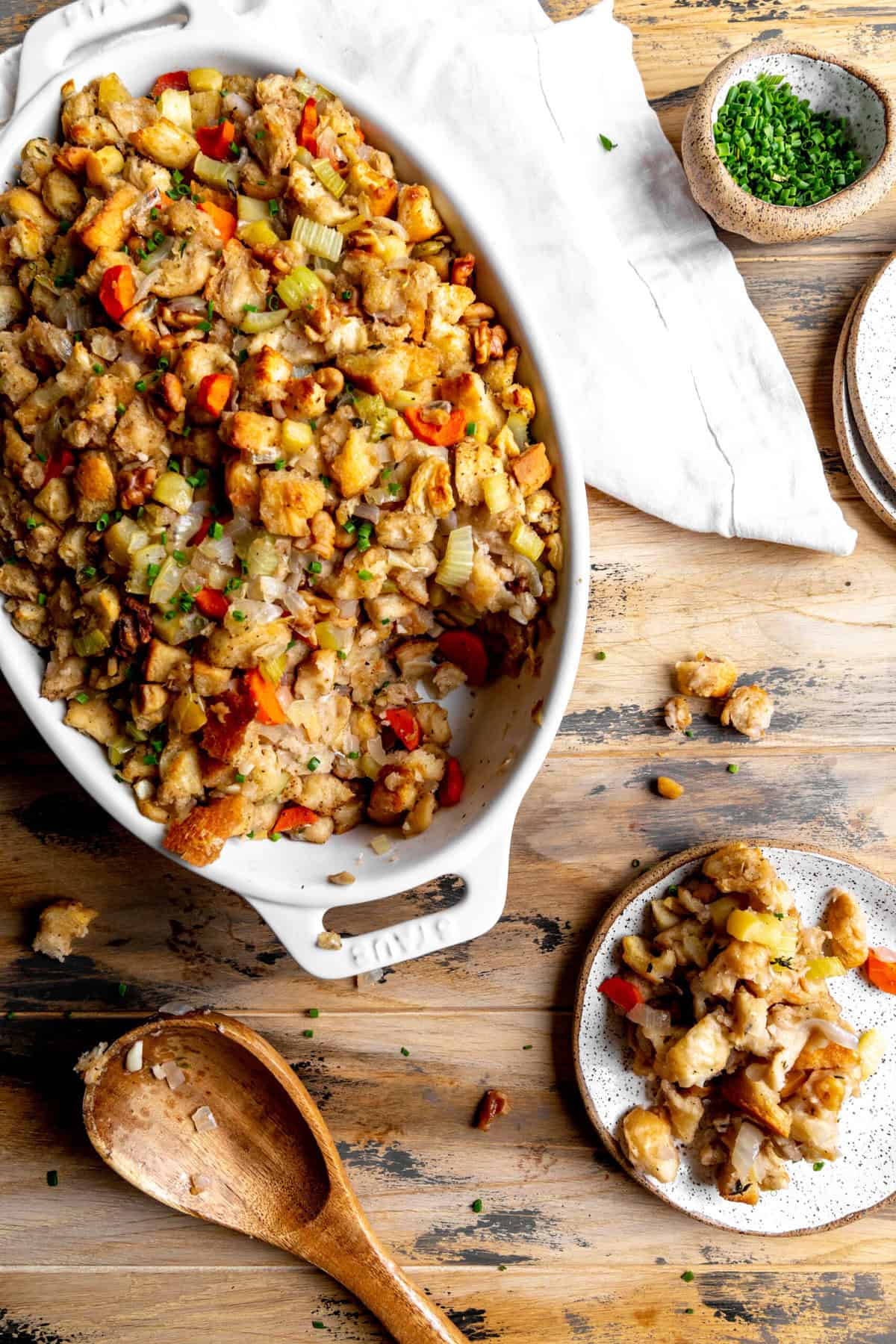 Dish of stuffing, a small plate of vegan stuffing and a wooden spoon.