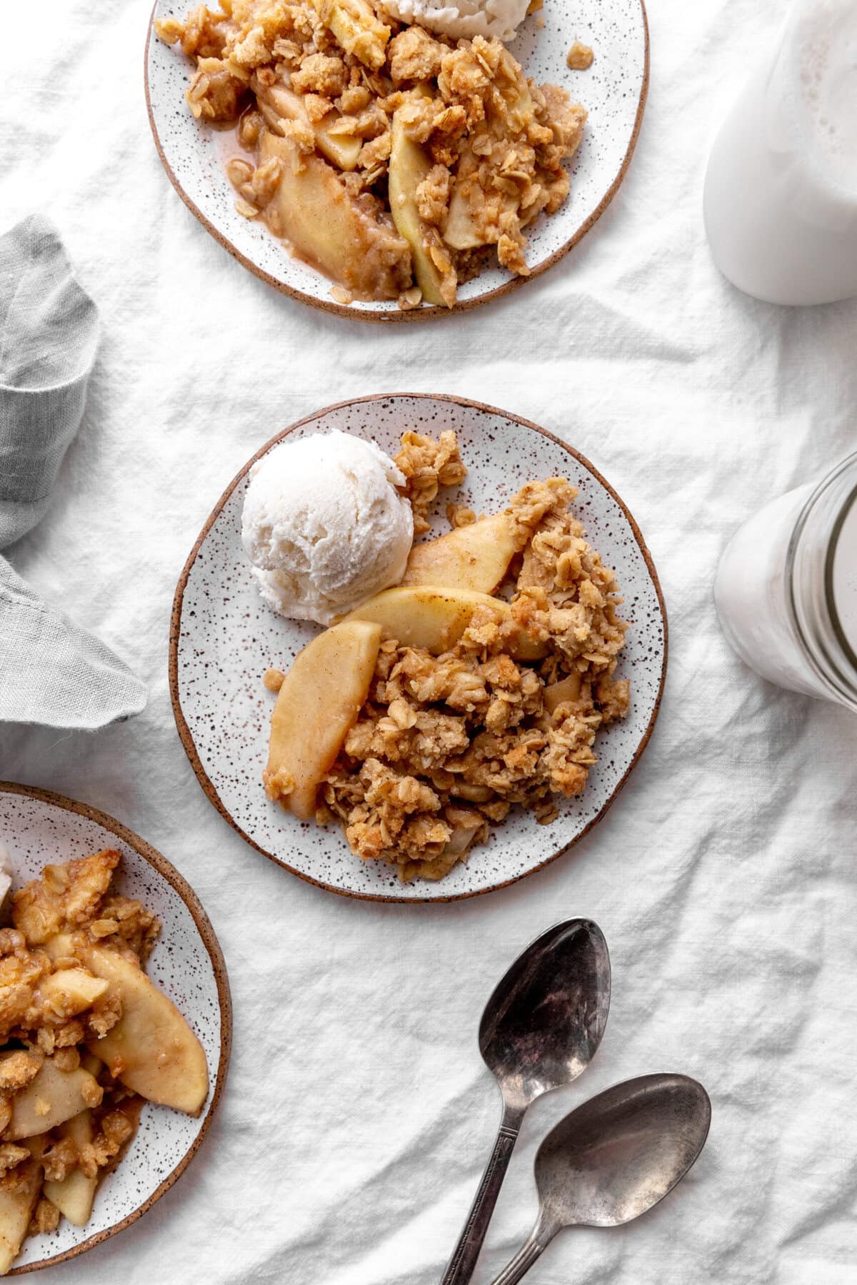 Apple crisp on white plates topped with a scoop of vanilla ice cream.