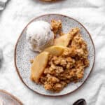 Serving of apple crisp on a plate with vanilla ice cream.