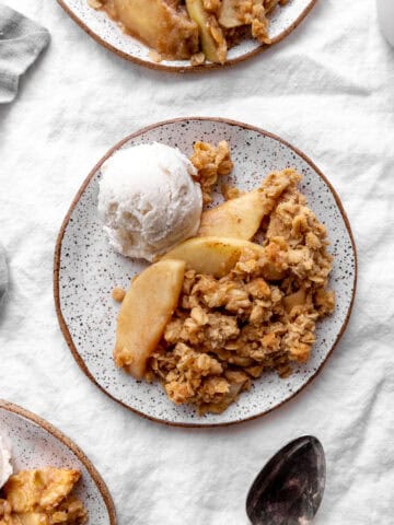 Serving of apple crisp on a plate with vanilla ice cream.