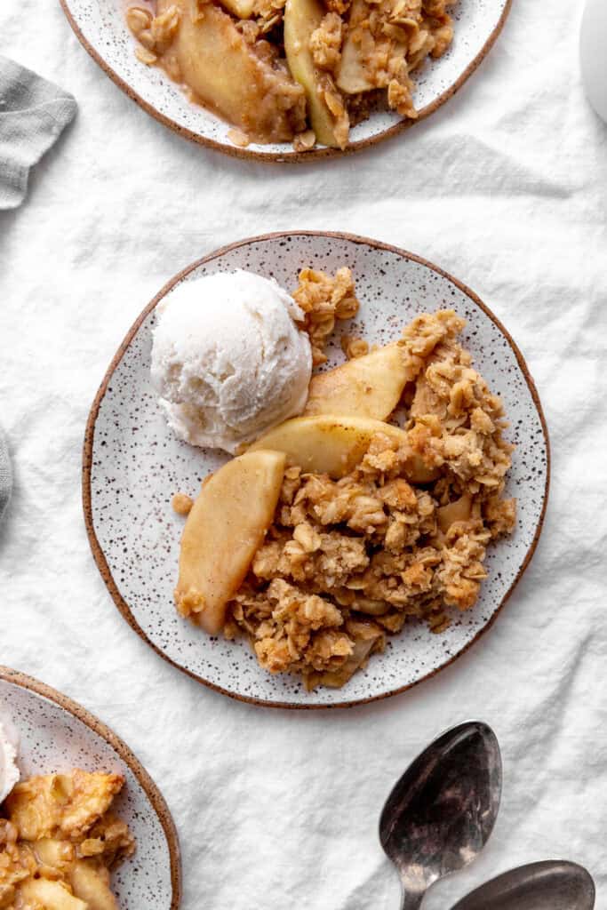 Serving of apple crisp on a plate with vanilla ice cream.