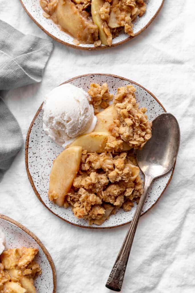 Serving of apple crisp on a plate with vanilla ice cream and a spoon.