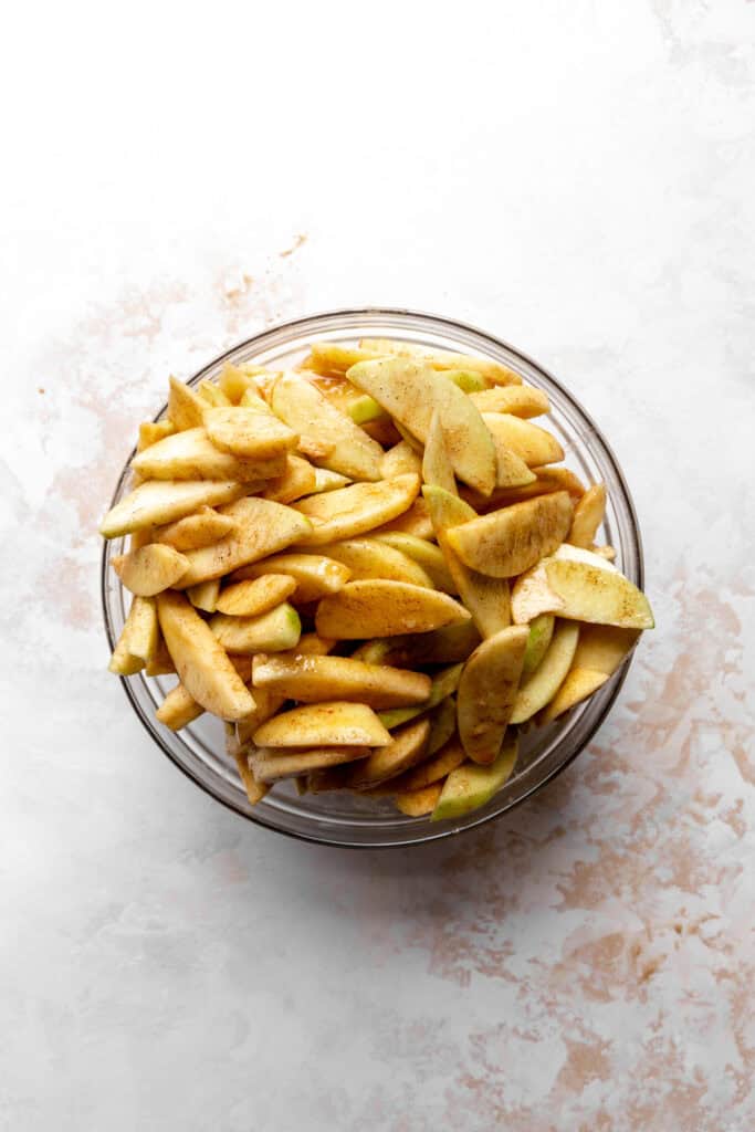 Glass bowl of apples slices tossed with sugar and spices.