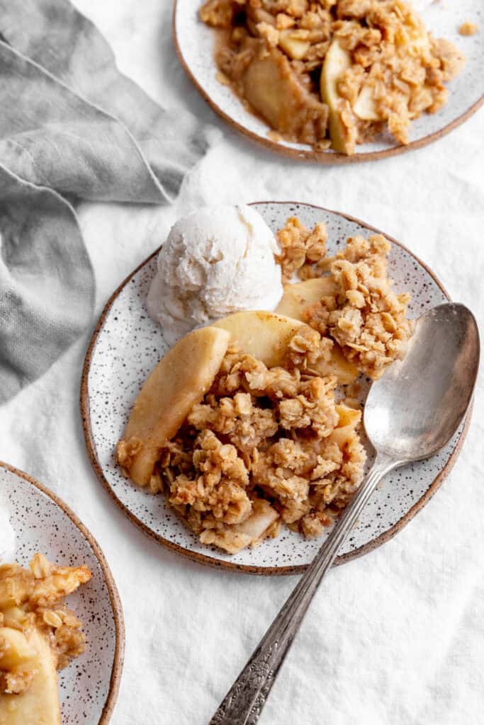 Apple crisp on a plate with vanilla ice cream and a spoon with a linen napkin.