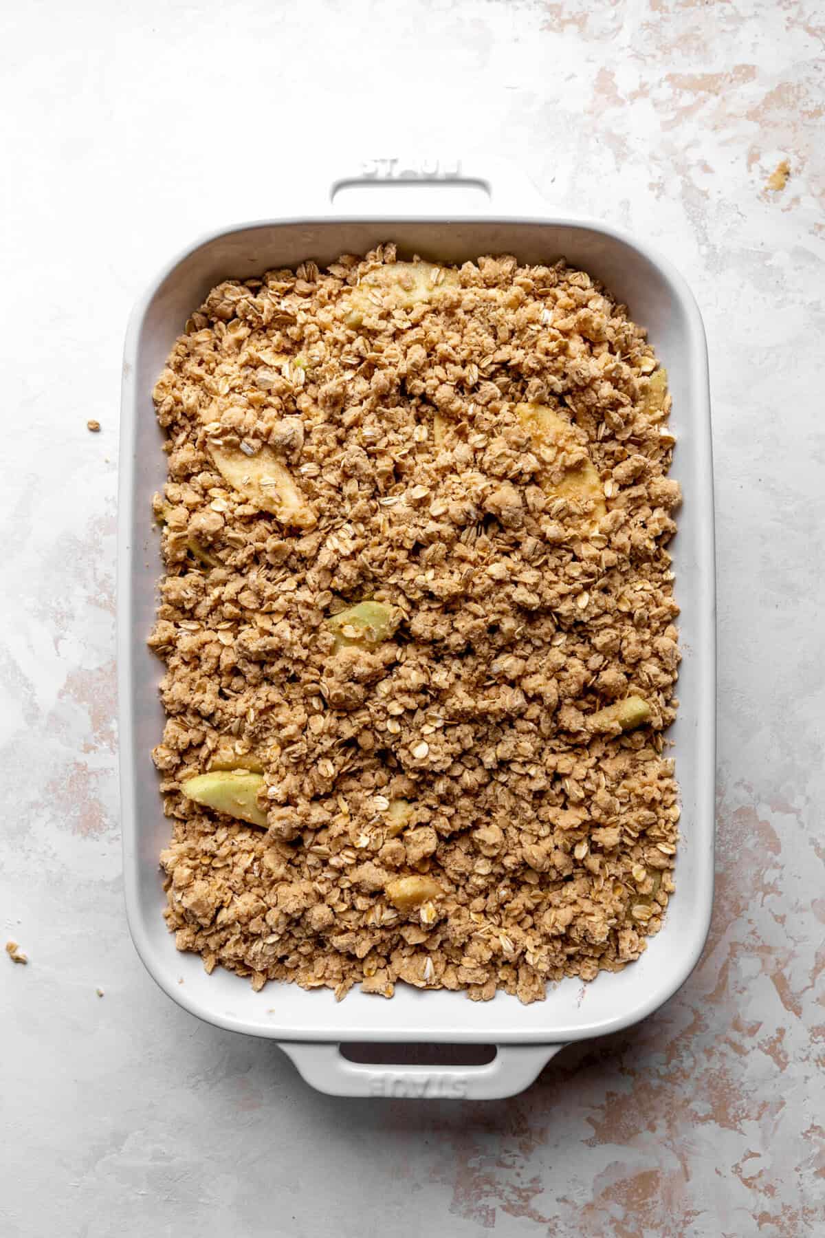 Unbaked apple crisp in a white dish.