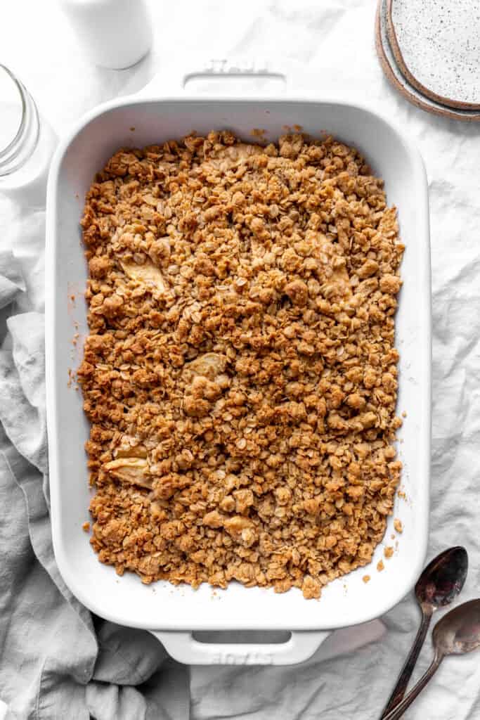 Baked apple crisp, a stack of white plates and a glass of milk.
