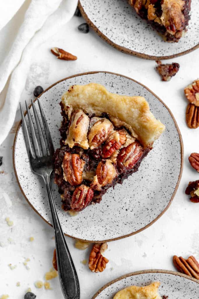 Slice of chocolate bourbon pecan pie on a white plate with a fork.