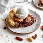 Slice of chocolate bourbon pecan pie topped with a scoop of vanilla ice cream.