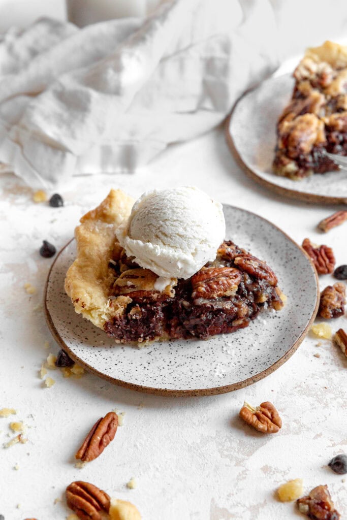 Slice of chocolate bourbon pecan pie topped with a scoop of vanilla ice cream and a napkin.