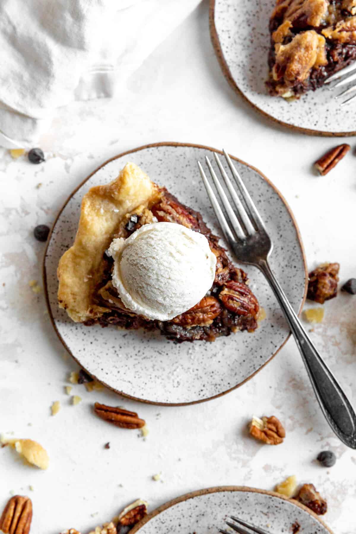 Slice of chocolate bourbon pecan pie topped with a scoop of vanilla ice cream and a fork.