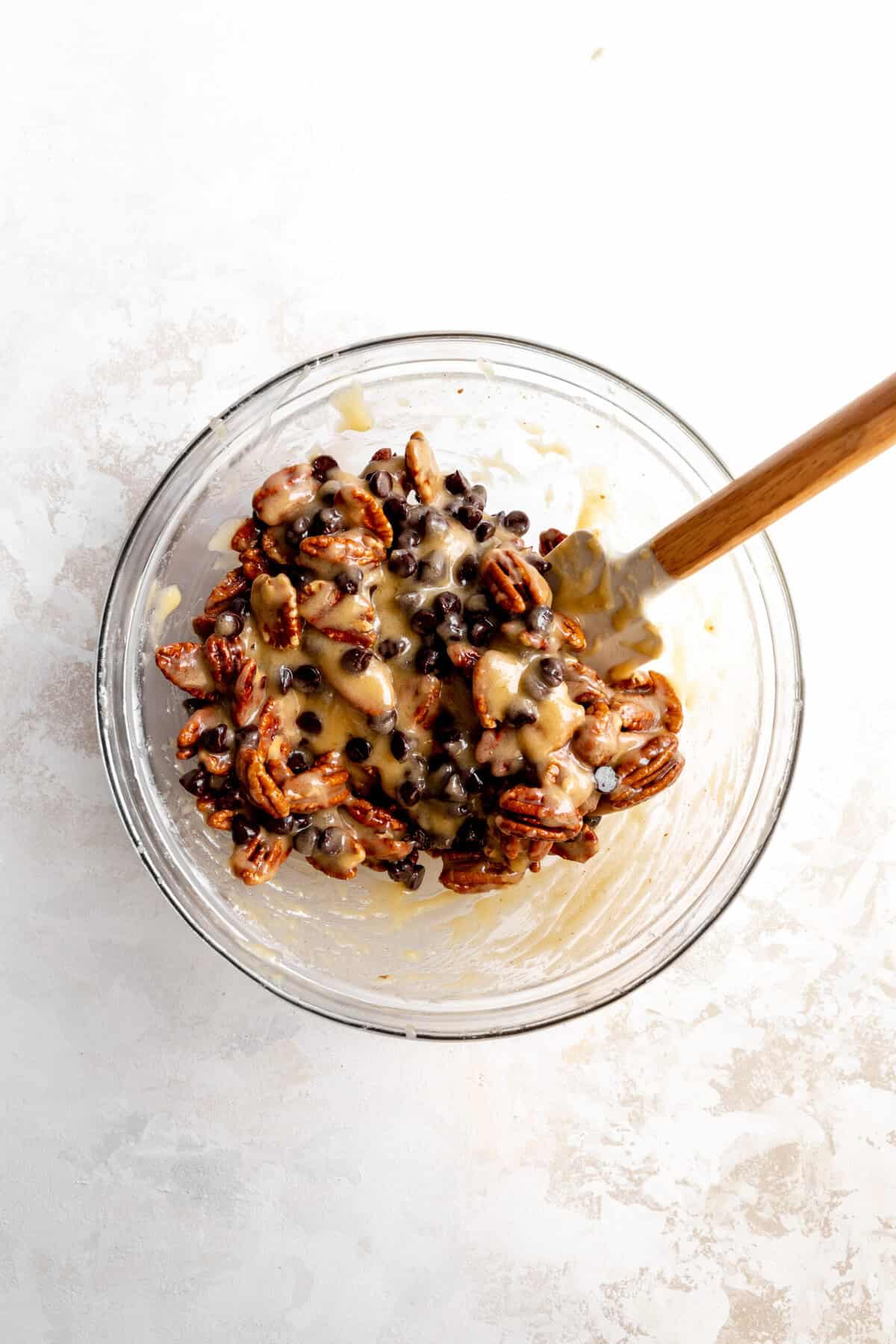 Chocolate pecan pie filling in a glass bowl with a rubber spatula.