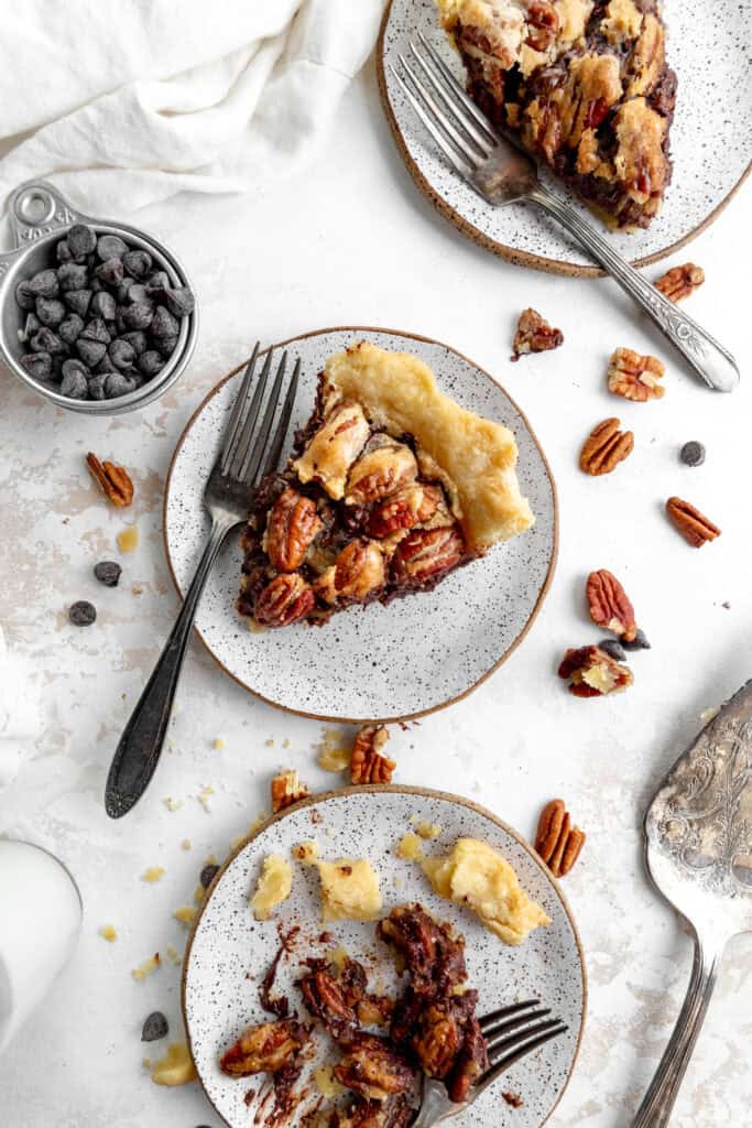 Three slices of chocolate pecan pie on plates and a cup of chocolate chip.