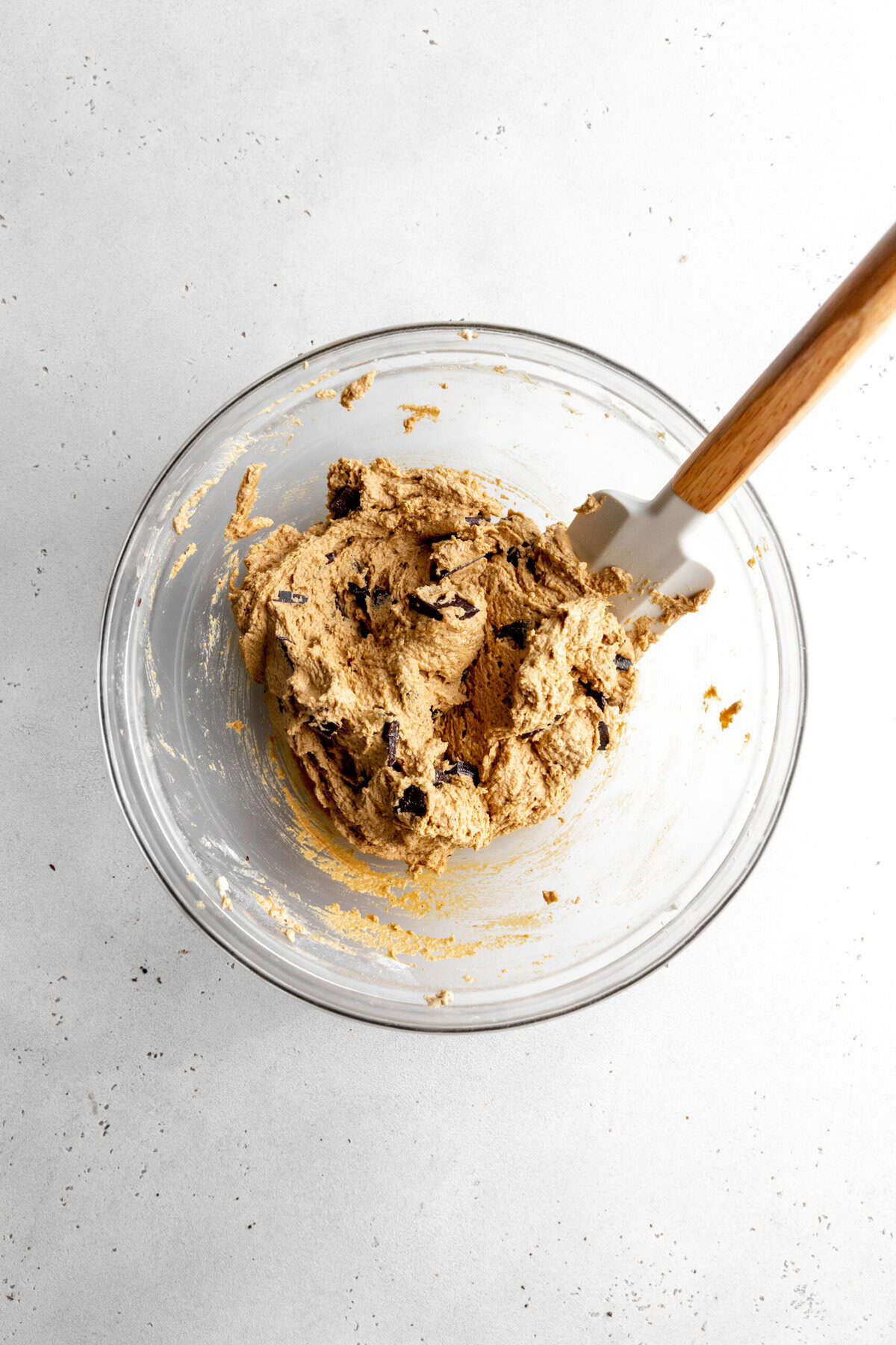 Glass bowl of chocolate chip cookies dough and a rubber spatula.