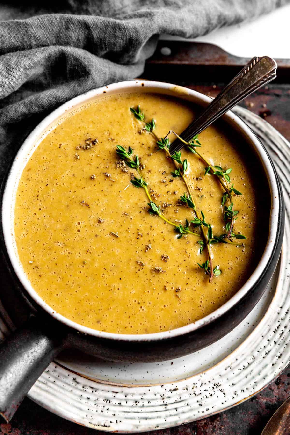 Spoon resting in a bowl of gravy topped with fresh thyme.