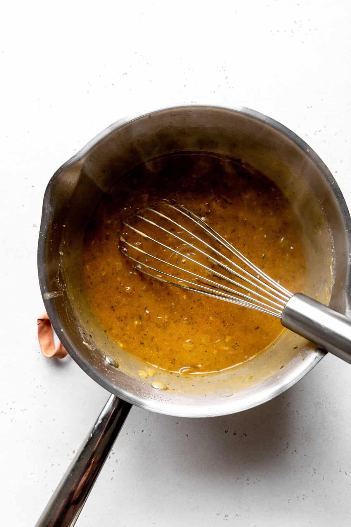 Gravy in a sliver saucepan with a wire whisk.
