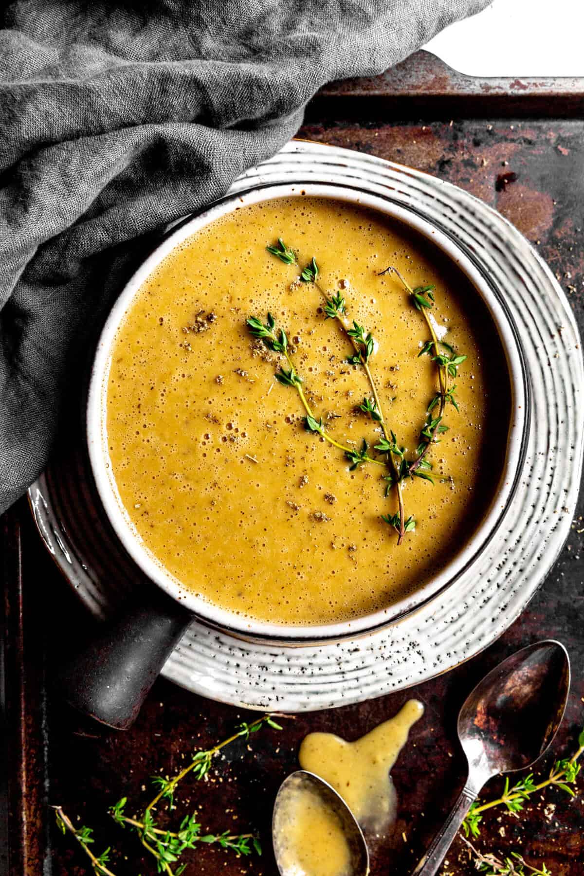 Bowl of gravy on a baking sheet with spoons and fresh thyme sprigs.