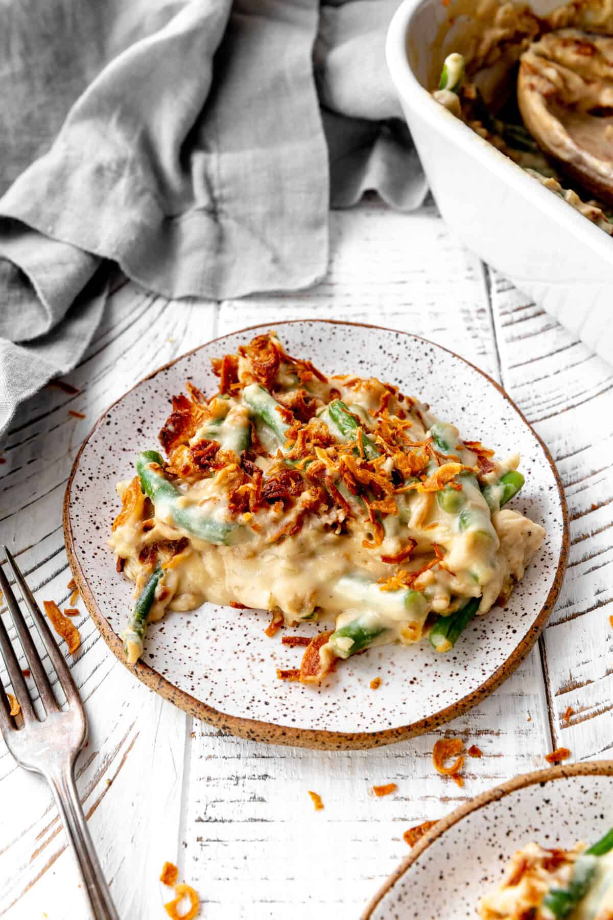 Plate of green bean casserole in front of a large green bean casserole dish.