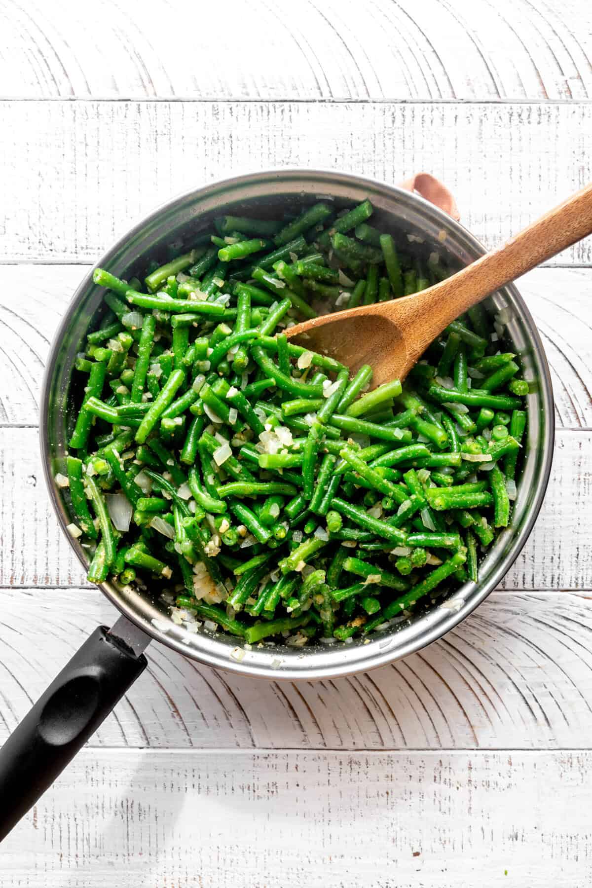 Sautéed green beans in a skillet with a wooden spoon.