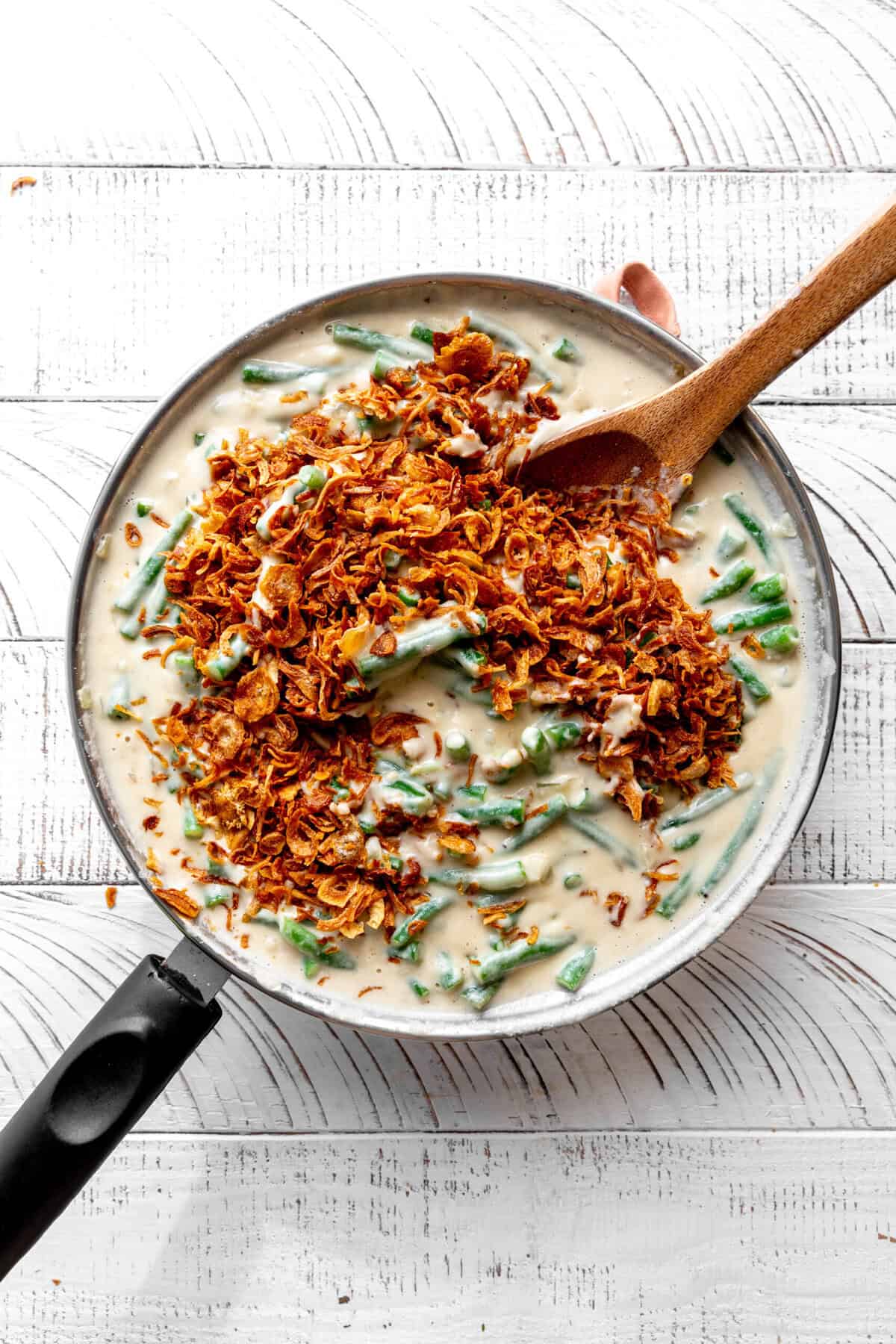 Green beans and cashew cream in a skillet covered with fried onions.