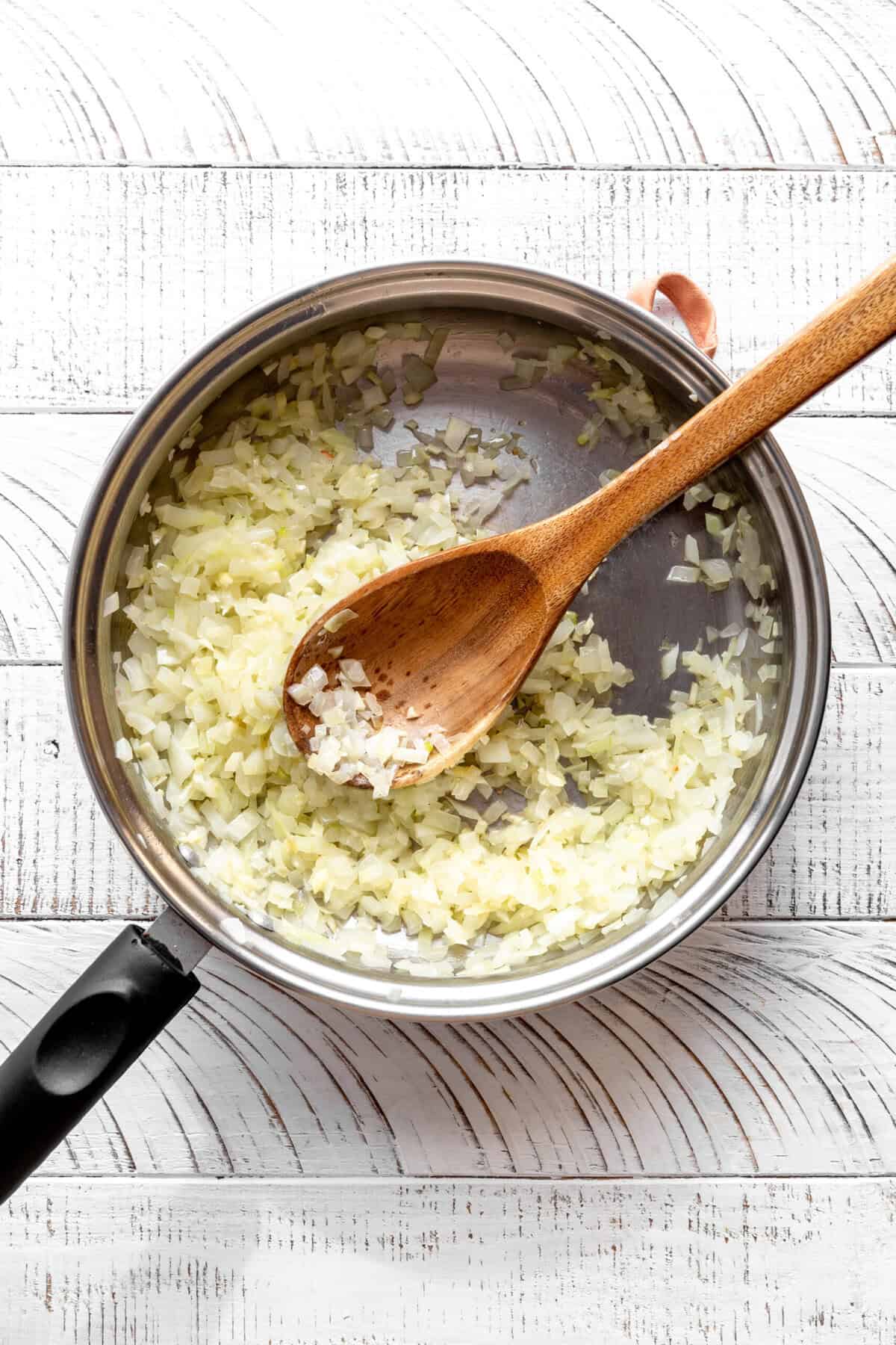 Sautéed onions in a skillet with a wooden spoon.