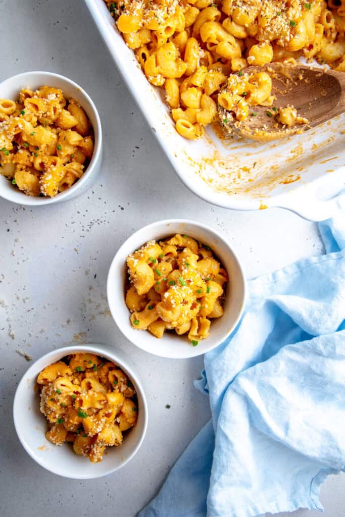 Three small bowls of mac and cheese and a casserole dish.