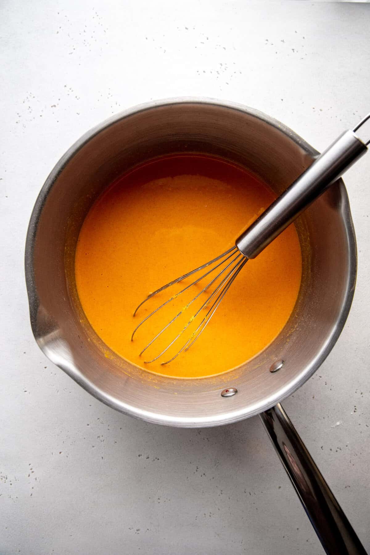 Saucepan of vegan mac and cheese sauce and a wire whisk.