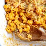 Wooden spoon digging into a dish of vegan mac and cheese.