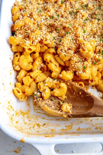Wooden spoon digging into a dish of vegan mac and cheese.