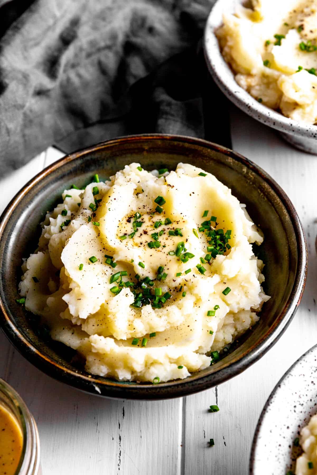 Bowl of mashed potatoes topped with butter and fresh chives.