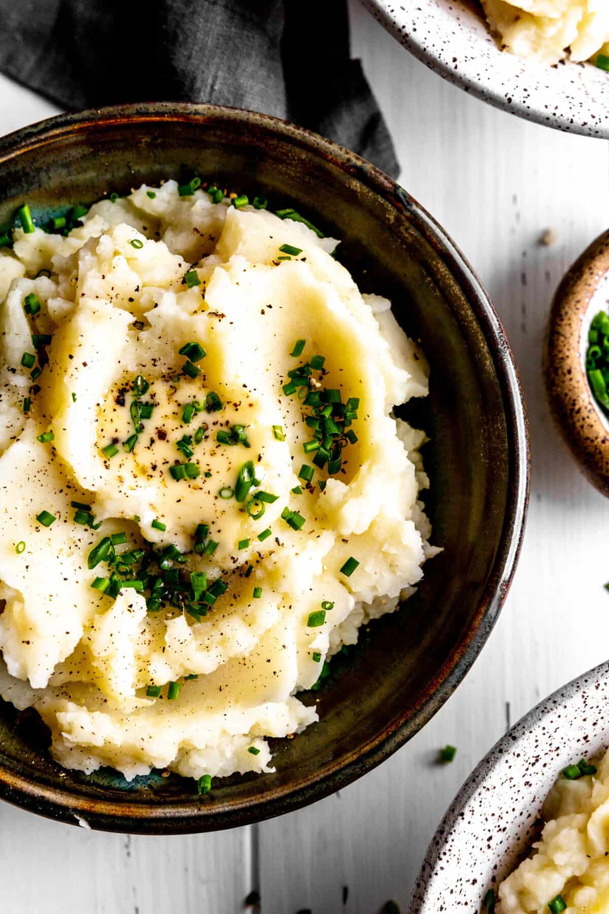 Bowl of mashed potatoes topped with butter and fresh chives.