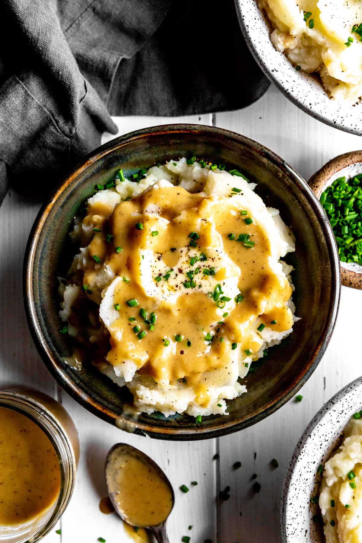Bowl of mashed potatoes covered in gravy and a small cup of gravy.