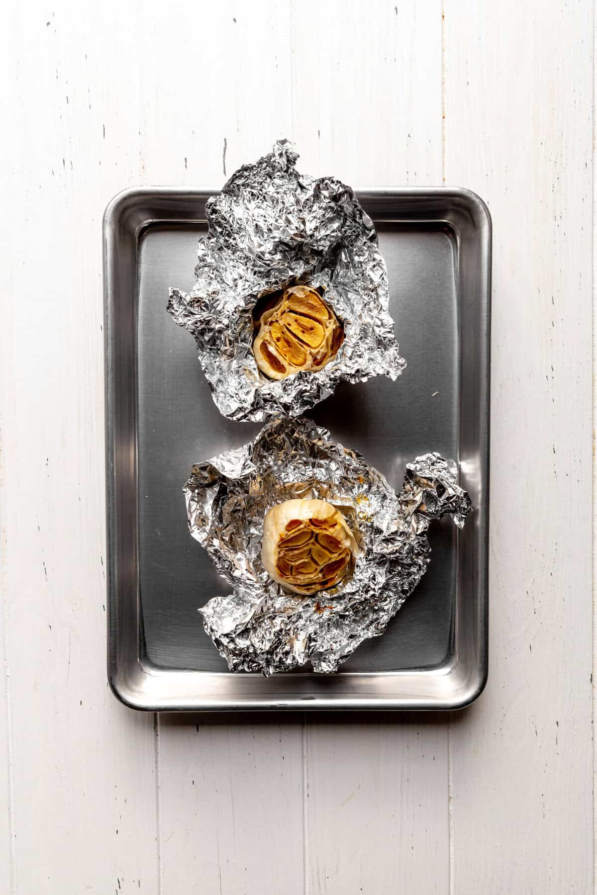 Heads of roasted garlic in tinfoil on a baking sheet.