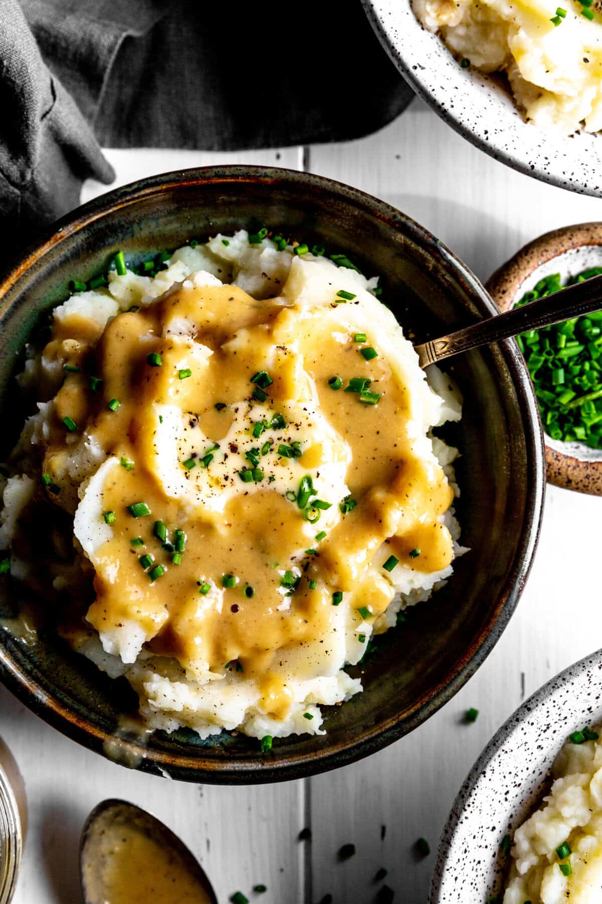 Spoon digging into a bowl of mashed potatoes covered in gravy.