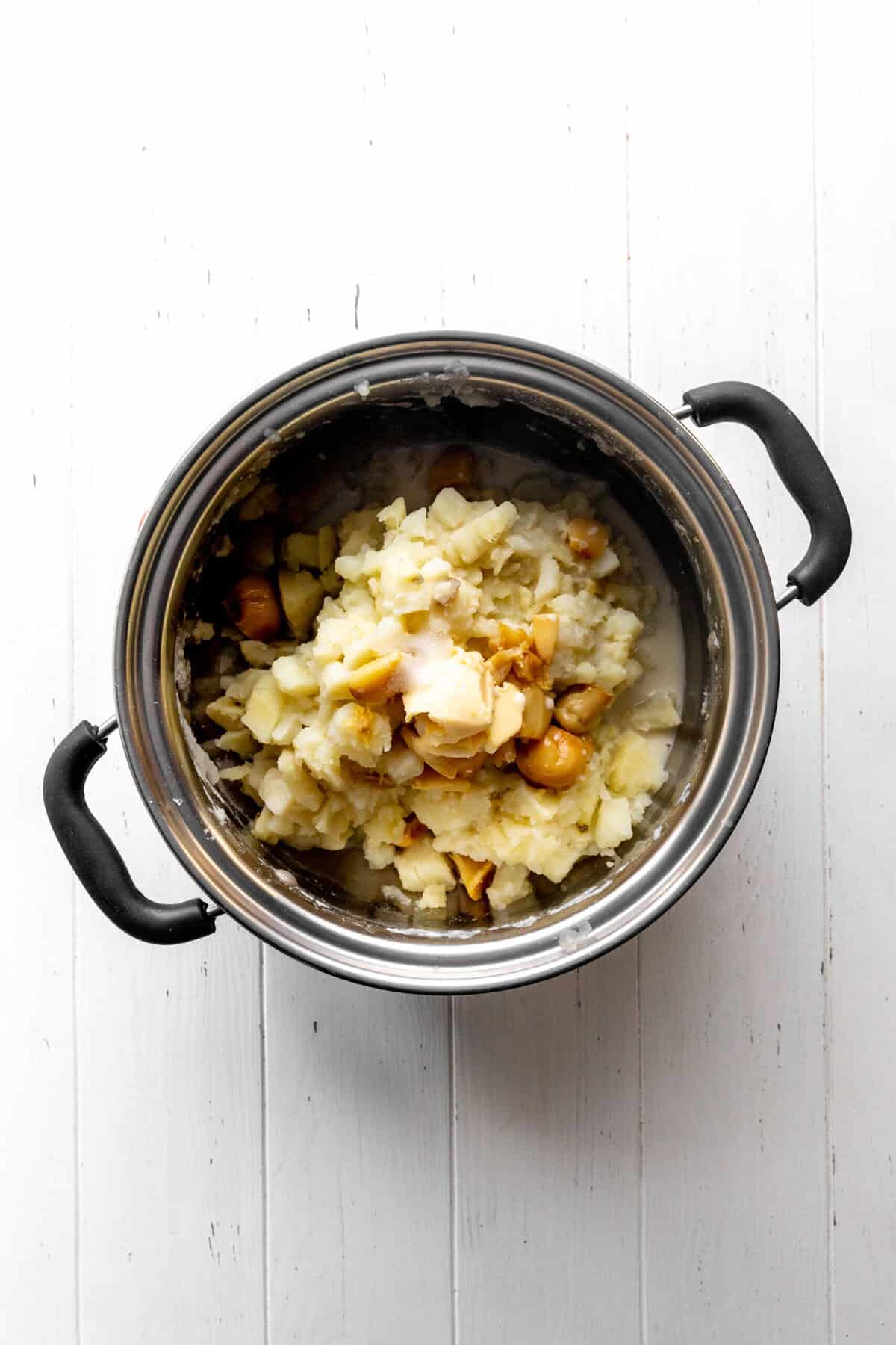 Pot of boiled potatoes, roasted garlic cloves, butter and milk.