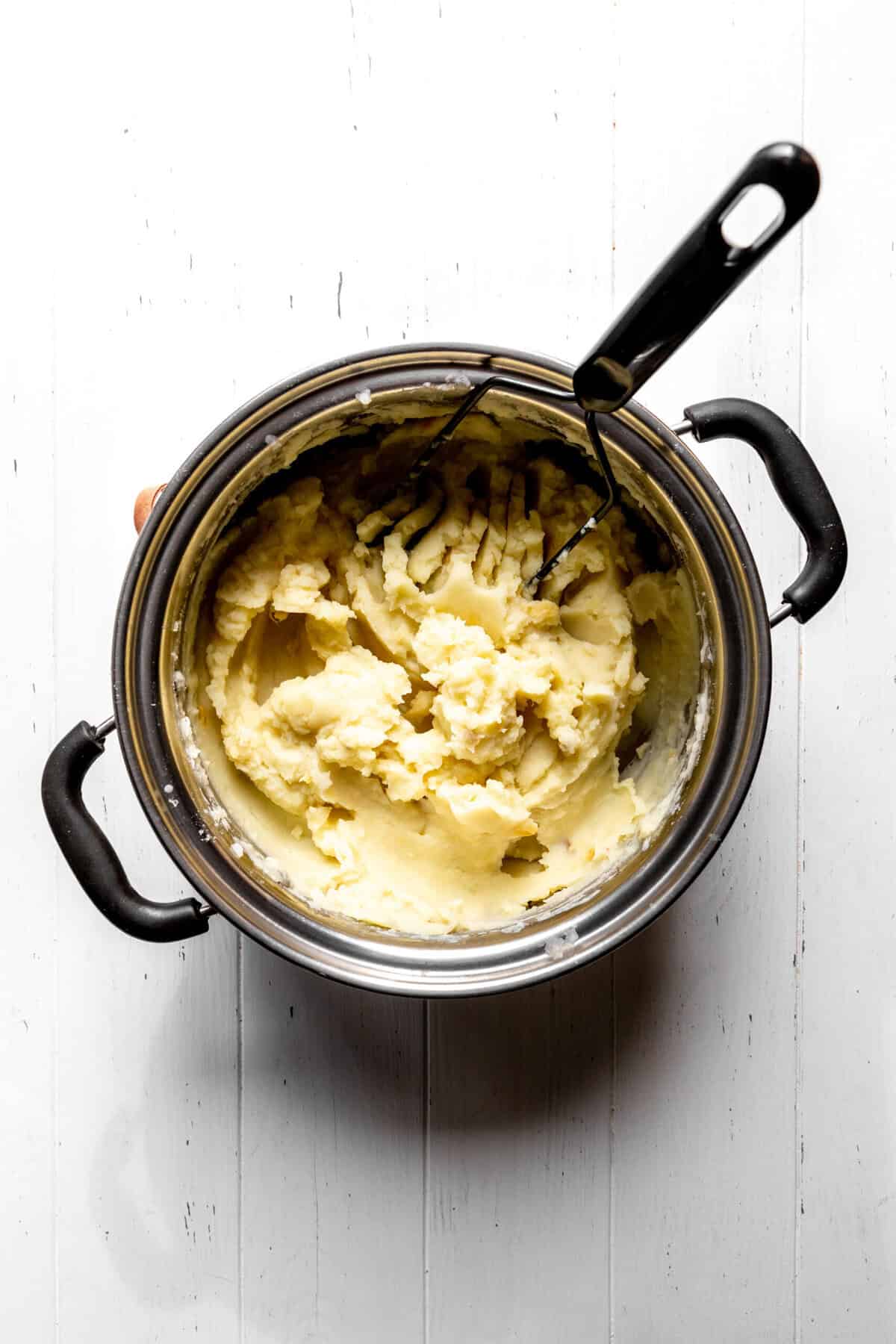 Pot of mashed potatoes and a potato masher.