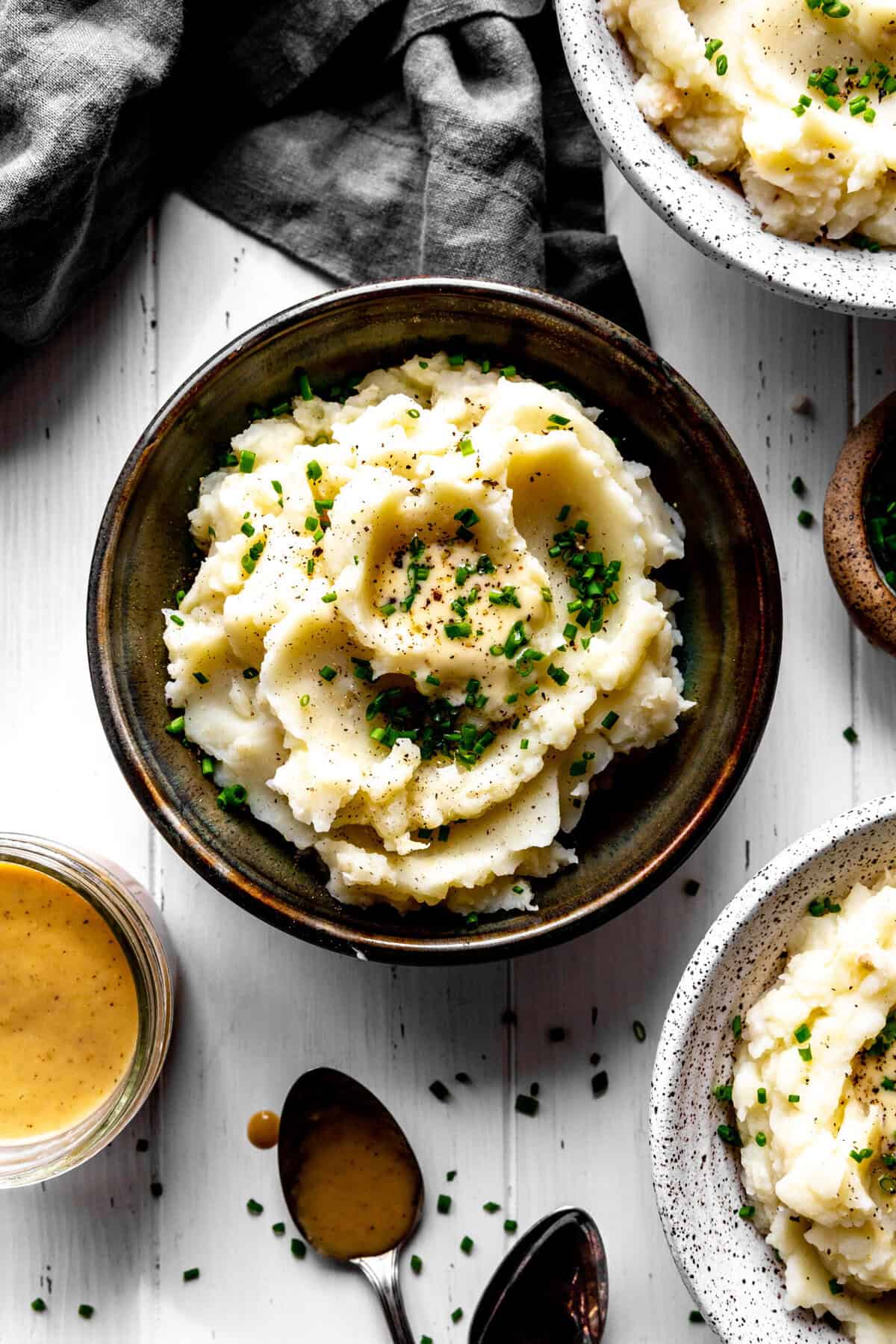 Bowl of mashed potatoes, small cup of gravy and two spoons.