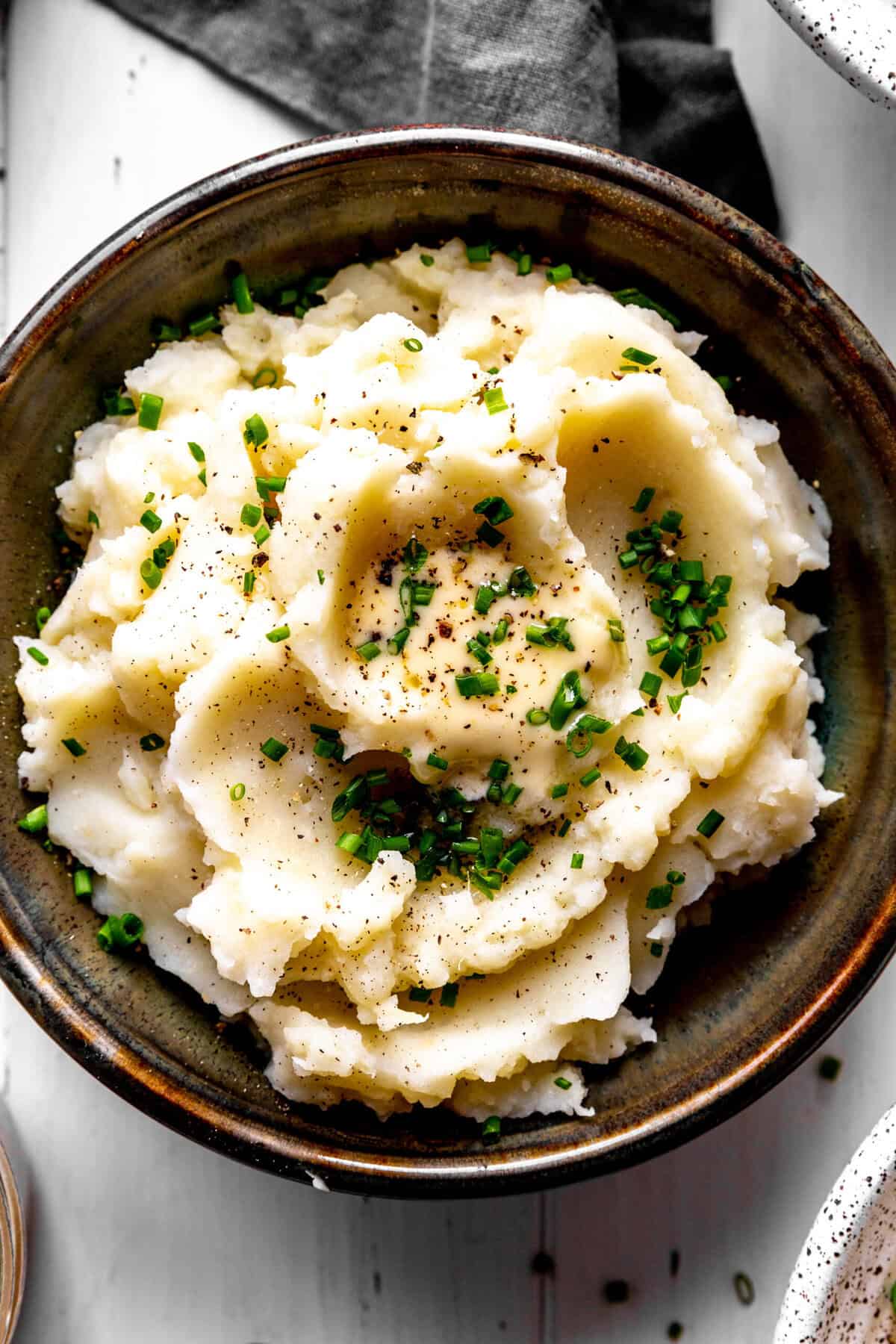 Bowl of mashed potatoes topped with butter and fresh chives.