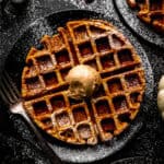 Pumpkin waffle topped with cinnamon butter on a black plate with a fork.