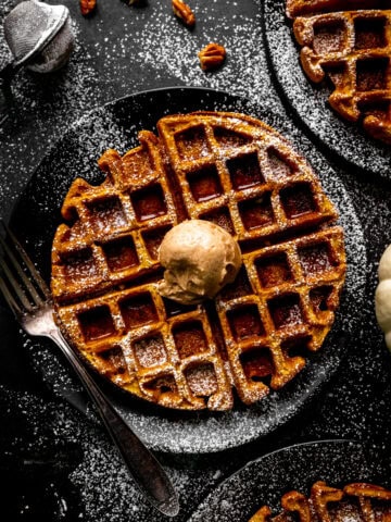 Pumpkin waffle topped with cinnamon butter on a black plate with a fork.