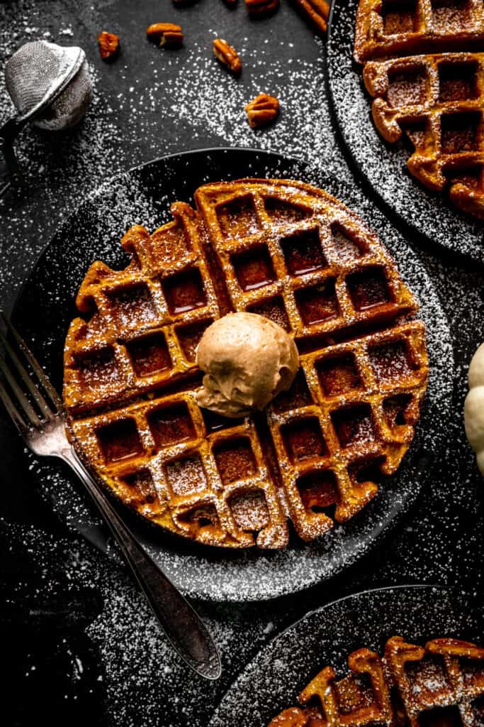 Pumpkin waffle topped with cinnamon butter on a black plate with a fork.
