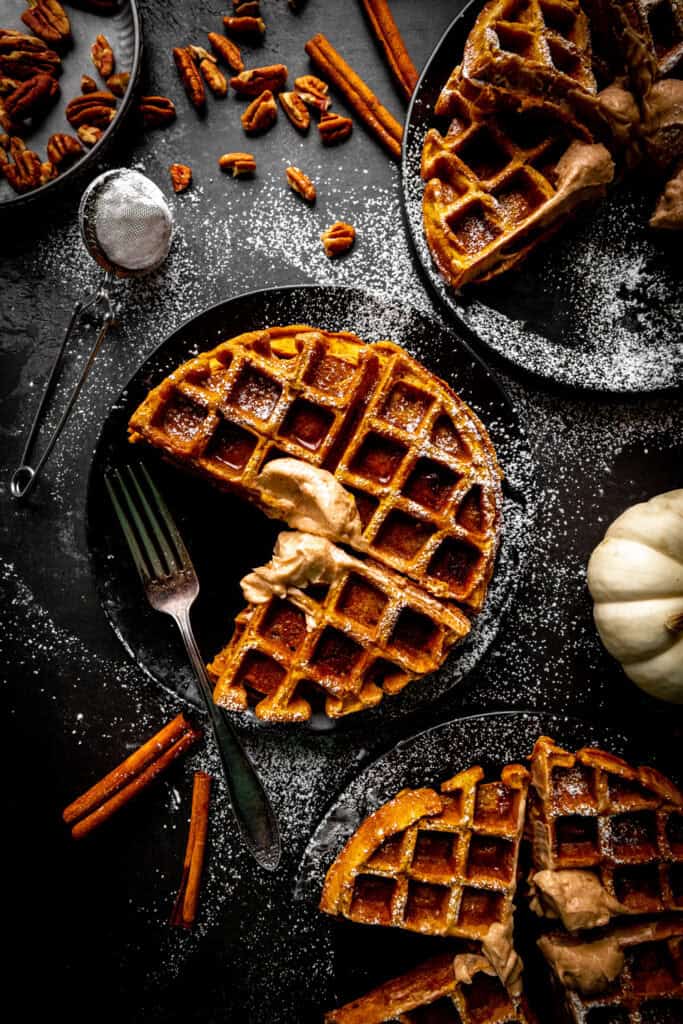 Pumpkin waffle sections on plates covered in powdered sugar and pecans.