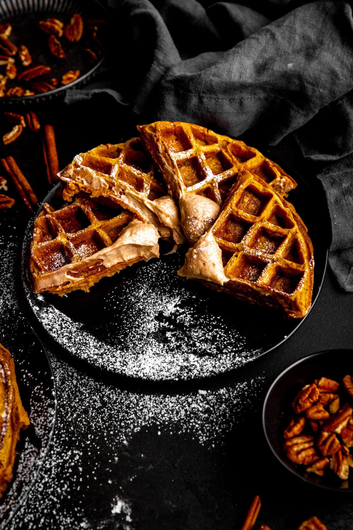 Four pumpkin waffle sections on a plate and a cup of pecan pieces.