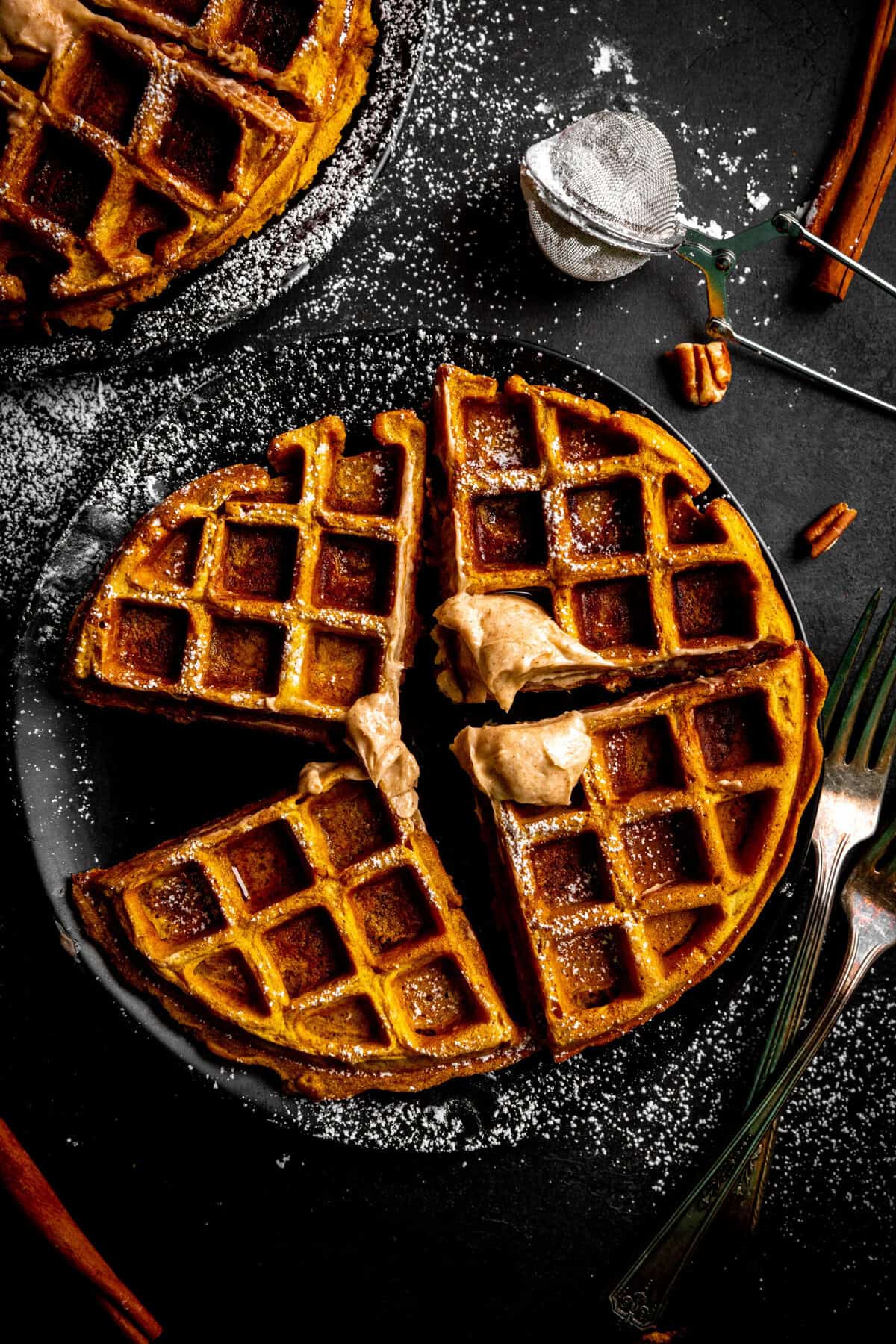 Four pumpkin waffle sections on a plate with powdered sugar.