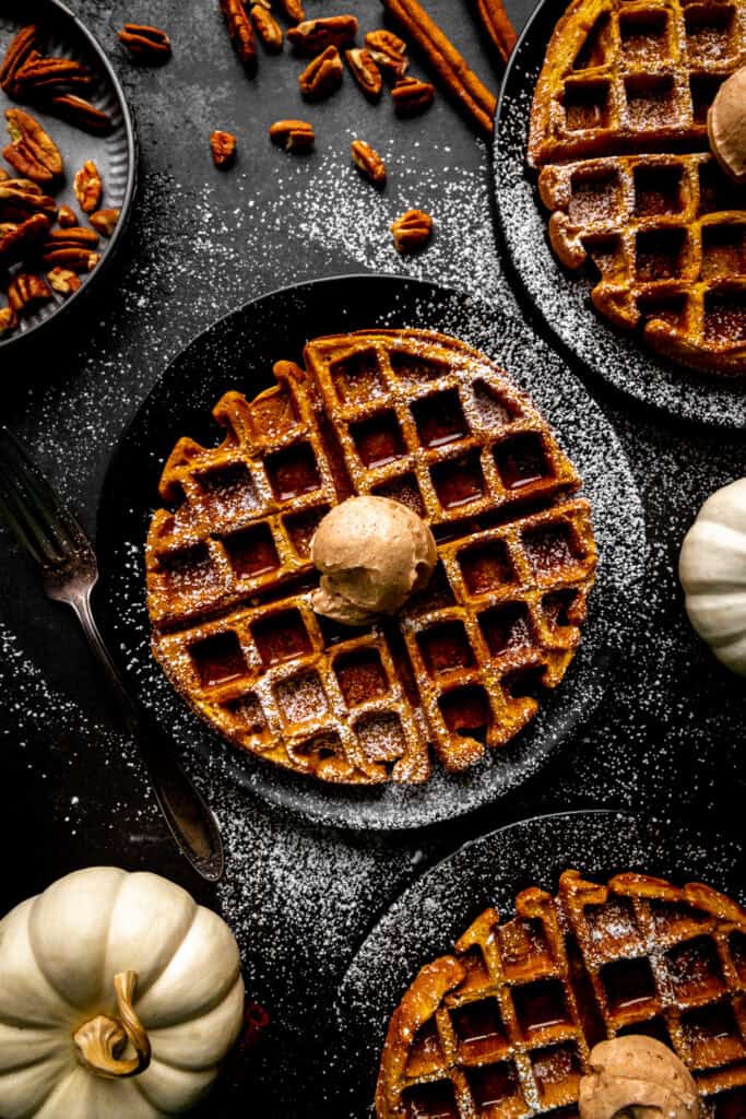 Three pumpkin waffles topped with a scoop of cinnamon butter.