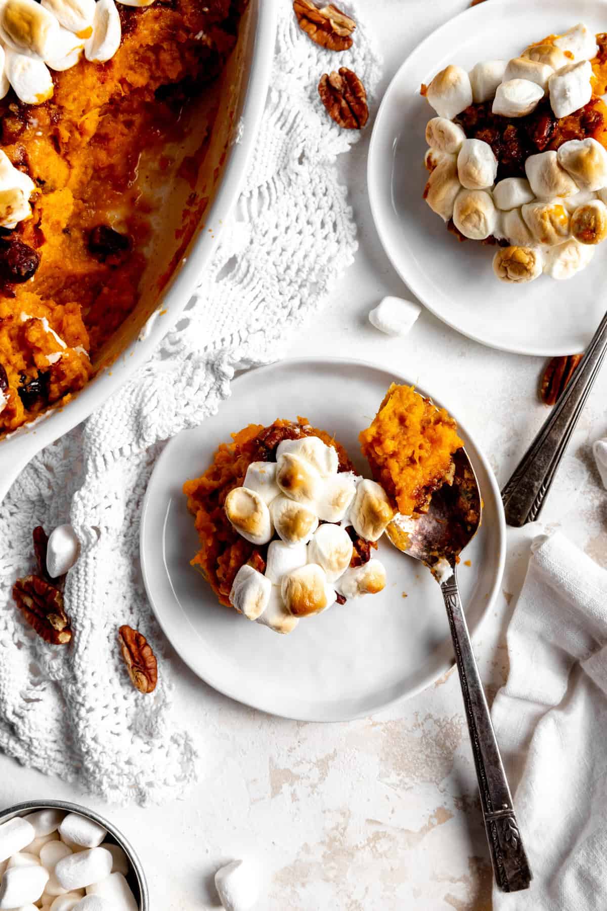 Spoon digging into a plate of sweet potato casserole on a white plate.