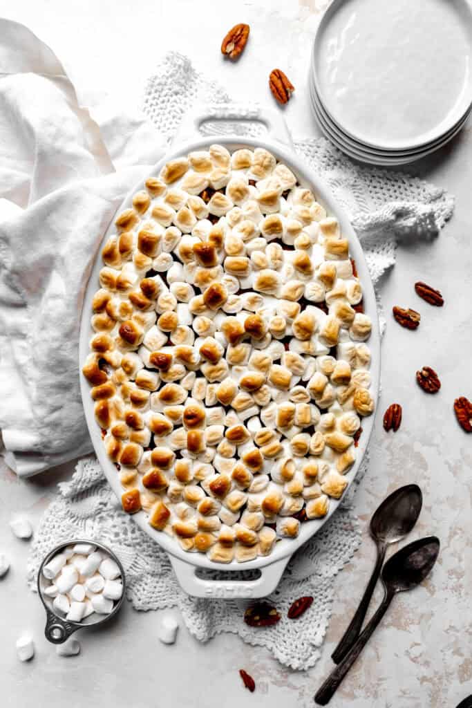 Baked sweet potato casserole, a stack of white plates and two spoons.